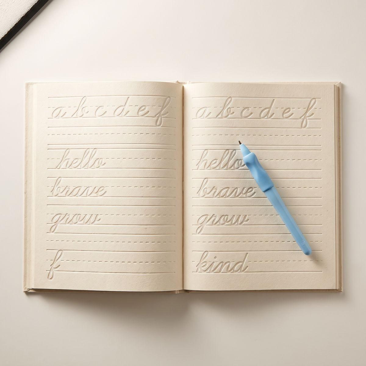 Cahier d'écriture cursive ouvert avec son stylo